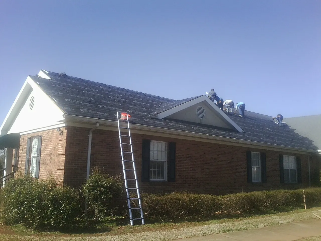 Crew tearing shingles off a brick ranch roof with a ladder set — Metal Roof Repair work by our crew in Isleton