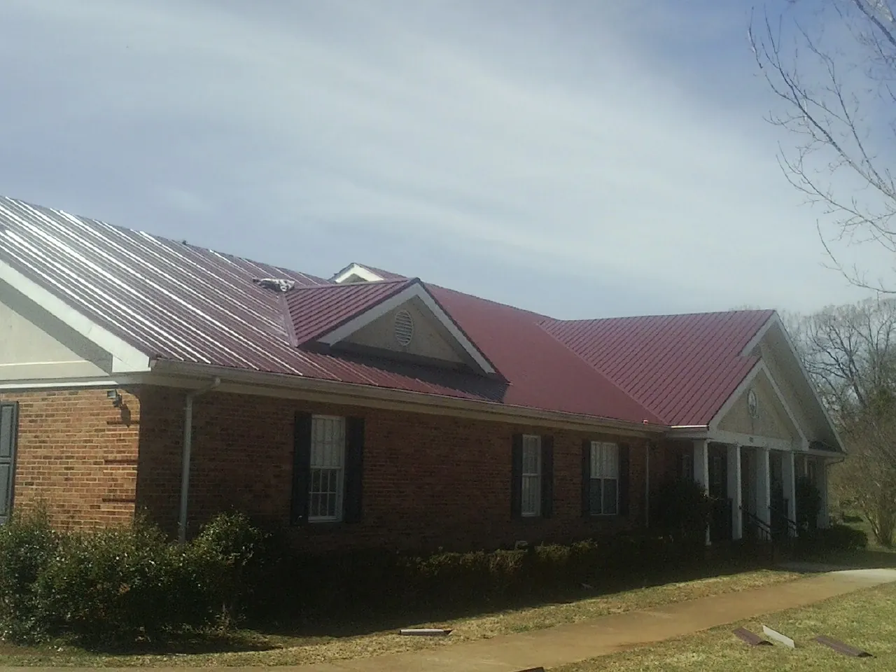 Red metal roof with gabled entries on a long brick building, from a Hail Damage Roof Repair job in Isleton